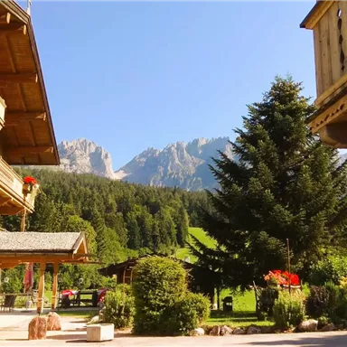 A picturesque mountain cabin with flower boxes, surrounded by trees. In the background, majestic mountains rise under a blue sky.