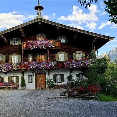 Ein traditionelles, charmantes Holzhaus mit bunten Blumenkästen an den Fenstern. Im Hintergrund sind grüne Wiesen und Berge zu sehen.