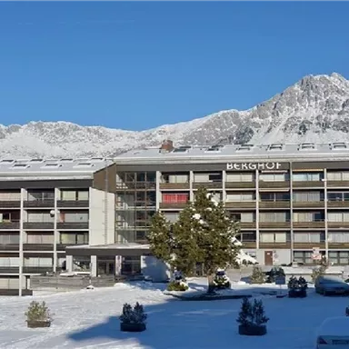 A modern hotel building in the snow, surrounded by mountains. The landscape is clear and sunny, with a peaceful atmosphere.
