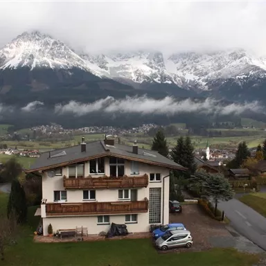 A modern house near a picturesque mountain landscape. The snow-covered mountains and the green valley create an impressive backdrop.