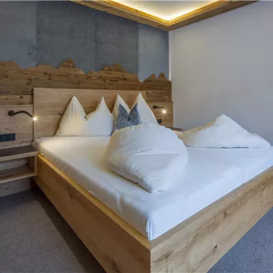 Ein modernes Schlafzimmer mit einem Holzbett und gemütlichen weißen Kissen. Die sanfte Beleuchtung sorgt für eine entspannte Atmosphäre.
