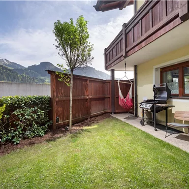 A cozy garden with a grill and seating. In the background, mountains can be seen and the sky is clear.