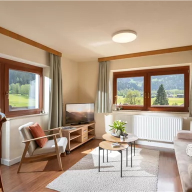 A cozy living room with large windows and a view of the landscape. The decor is modern and inviting, with a sofa and a small table.