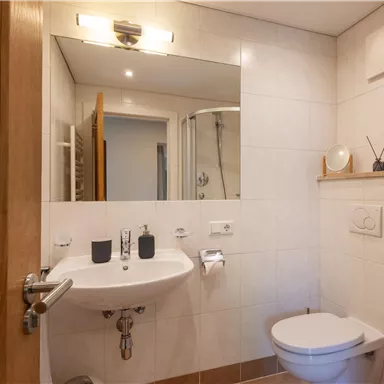 A modern bathroom with a sink, a mirror, and a shower. It is bright and clean, with a minimalist decor.