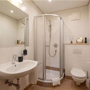 A modern bathroom with a shower, a sink, and a toilet. The walls are brightly tiled and there is a comfortable decor.