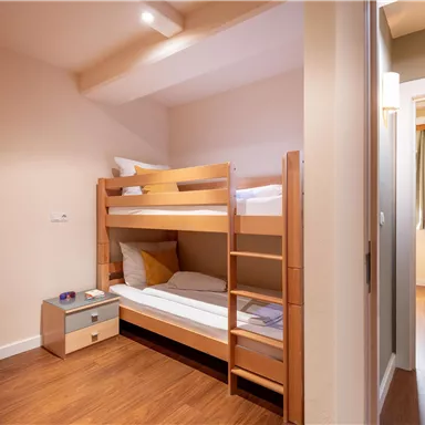 A small room with a bunk bed and a nightstand. The room has a bright and modern style with wooden flooring.