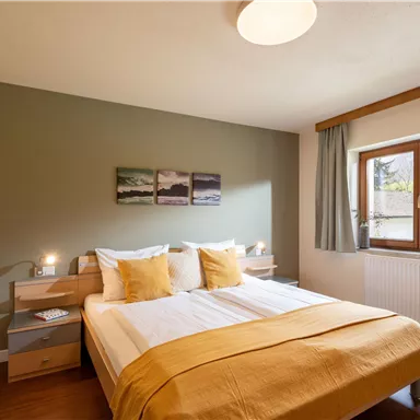 A modern bedroom with a large bed and yellow pillows. The walls are painted in calming tones, and there is a window with a view of the outdoors.