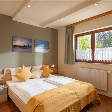 A cozy bedroom with a double bed and elegant bed linen. The room has large windows and minimalist decoration on the walls.
