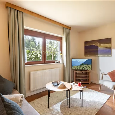 A cozy living space with a bright sofa and a small table. Large windows let in plenty of light and offer a view of the greenery.