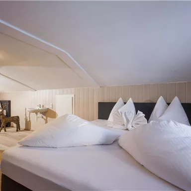 A cozy bedroom in the attic with two beds and white pillows. There is a small table and a chair in the room.