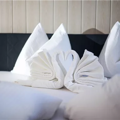A bed with white pillows and folded towels shaped like swans. The decoration conveys a romantic and inviting atmosphere.
