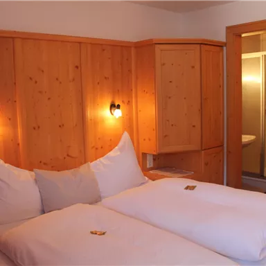 A cozy bedroom with two beds and wooden paneling. In the background, there is a modern bathroom with a shower.