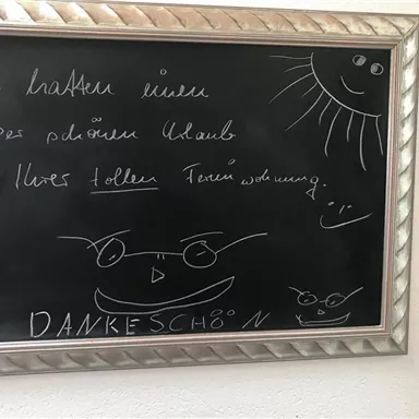 Ein schwarzes Brett mit freundlicher Nachricht und Zeichnungen. Der Text bedankt sich für einen schönen Aufenthalt in einer Ferienwohnung.