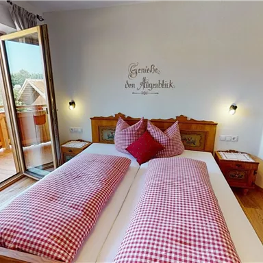Ein gemütliches Schlafzimmer mit einem großen Fenster und Zugang zum Balkon. Die Betten sind mit roten karierten Kissen dekoriert.