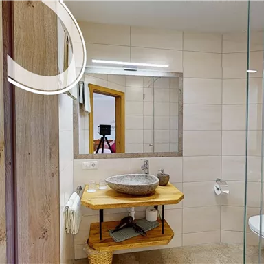 Ein modernes Badezimmer mit einem großen Spiegel und einer eleganten Waschschüssel auf einem Holzregal. Die Wände sind hell gefliest und die Einrichtung ist schlicht und ansprechend.