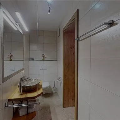 Ein modernes Badezimmer mit weißen Fliesen und Holzdetails. Es verfügt über ein Waschbecken, einen Spiegel und eine Toilette.