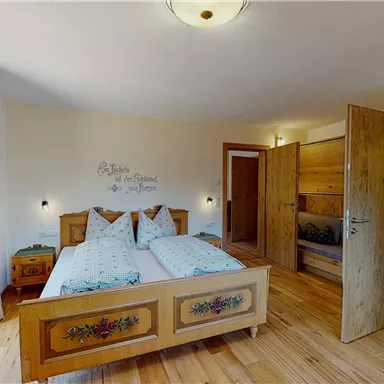 Ein gemütliches Schlafzimmer mit Holzfußboden und einem großen Bett. Die Wände sind hell gestrichen und mit einem charmanten Wanddesign dekoriert.