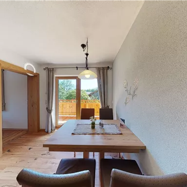 Ein heller Essbereich mit einem Holzstisch und gemütlichen Stühlen. Im Hintergrund sind Fenster mit Blick ins Freie.