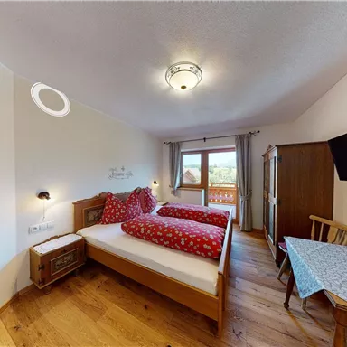 Ein gemütliches Schlafzimmer mit zwei Einzelbetten und rot gemusterten Bettdecken. Der Raum verfügt über ein Fenster mit Aussicht und eine kleine Sitzecke.