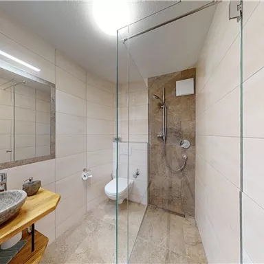 Ein modernes Badezimmer mit einer Glasdusche und einem stilvollen Waschbecken. Die Wände sind neutral gefliest und schaffen eine helle, einladende Atmosphäre.