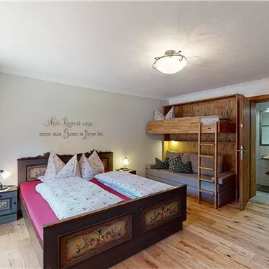Ein gemütliches Schlafzimmer mit einem Doppelbett und einem Etagenbett. Die Holzdecke und der Holzboden verleihen dem Raum eine warme Atmosphäre.