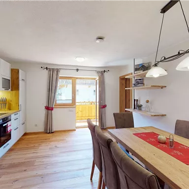 Eine moderne Küche mit einem Essbereich aus Holz. Es gibt große Fenster, die viel Tageslicht bieten.
