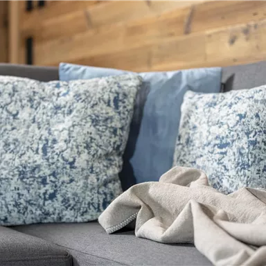 A cozy sofa with decorative cushions in shades of blue and gray. On it lays a light blanket that creates an inviting atmosphere.