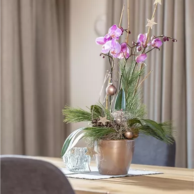 A table with a decorative flower arrangement in a pot. In the background, curtains and chairs can be seen.