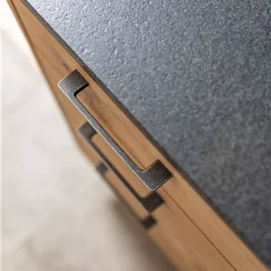 A modern kitchen surface made of dark material with a wooden cabinet and a stylish handle. The combination of wood and stone looks elegant and contemporary.