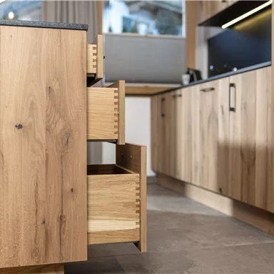 A modern kitchen with wooden furniture and open drawers. The space is bright and inviting, with a minimalist design.