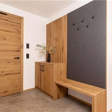 A modern entrance area with wood paneling and a simple seating option. The walls are light, and the overall impression is friendly and inviting.