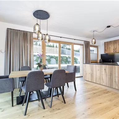 A modern kitchen with a wooden dining area and stylish chairs. Large windows let in plenty of daylight and offer a view of the outdoor terrace.