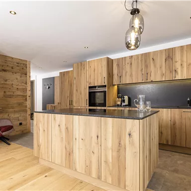 A modern kitchen with wooden furniture and a spacious cooking island. It features stylish lighting and has a warm, welcoming atmosphere.