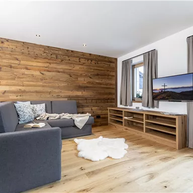 A modern living room with wood paneling and a cozy sofa. The room is bright and inviting, equipped with a television and a window with curtains.