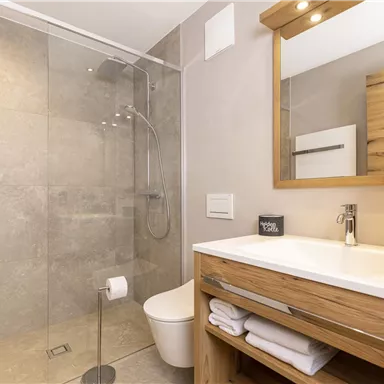 A modern bathroom with a glass shower and a wooden sink. Fresh towels and stylish lighting are available.