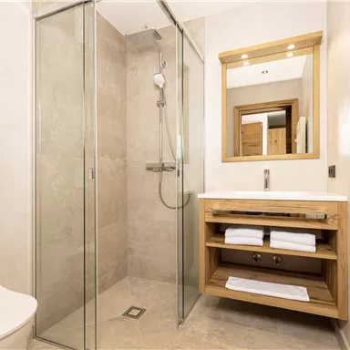 A modern bathroom with a glass shower and a wooden sink. There are towel racks and a large mirror.