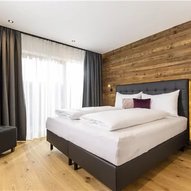 A modern room with a large bed and wood paneling. Large windows let in plenty of light.