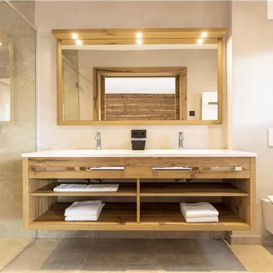 A modern bathroom with a wooden vanity unit and large mirrors. The shower is open, and the space feels bright and inviting.