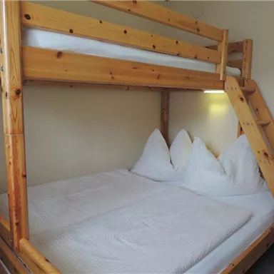 A simple wooden bunk bed with two mattress-supported sleeping places. The bedding is clean and tidy, and there are two large pillows.