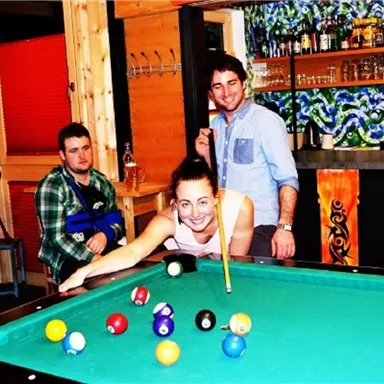 A sociable gathering at the billiard table with smiles and fun. In the background, a bar with colorful bottles can be seen.