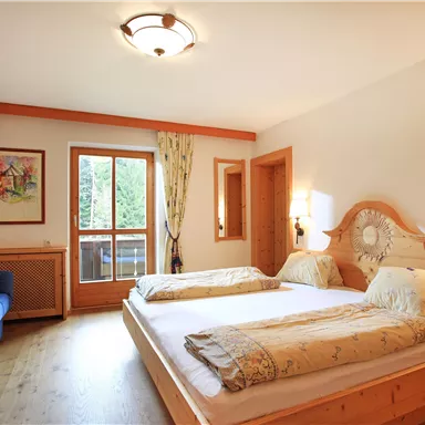 A cozy hotel room with two beds, a blue sofa, and a television. There are large windows overlooking nature and a warm, inviting atmosphere.