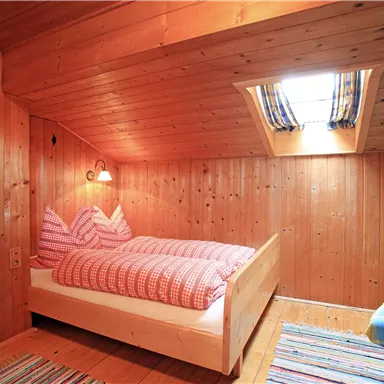 A cozy room with wood paneling and a double bed. There is a window with curtains and a colorful seating area.