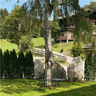 A quiet garden with a birch tree and several stones. In the background, green hills and a building can be seen.