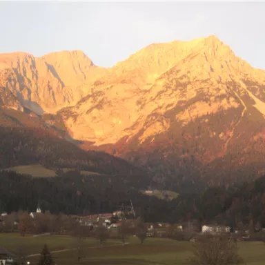 Ein majestätisches Gebirge bei Sonnenuntergang. Die Berge sind in warmes Licht gehüllt und die Landschaft wirkt friedlich.