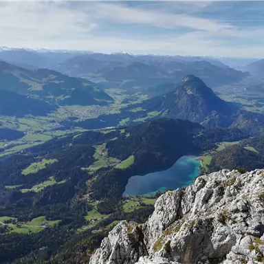 A picturesque landscape with mountains and green meadows. In the foreground, there are rocks, while in the background, a clear lake and more mountains can be seen.