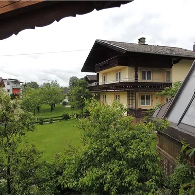 A picturesque residence surrounded by green trees and meadows. In the background, the mountains can be seen under a cloudy sky.