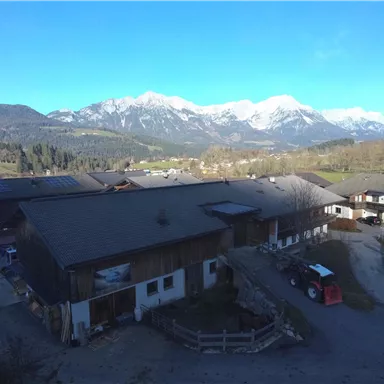 Eine ländliche Szenerie mit Gebäuden und einem klaren blauen Himmel. Im Hintergrund sind majestätische Berge zu sehen.