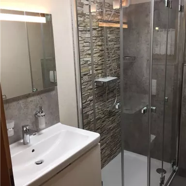 A modern bathroom with a glass shower and a stylish sink. The walls are clad in natural stone, and the lighting feels warm and inviting.