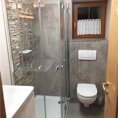 A modern bathroom with a shower, sink, and toilet. Stone wall covering and a window provide natural light.