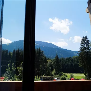 A beautiful view of mountains and green forests from a window. The sky is clear with some clouds.